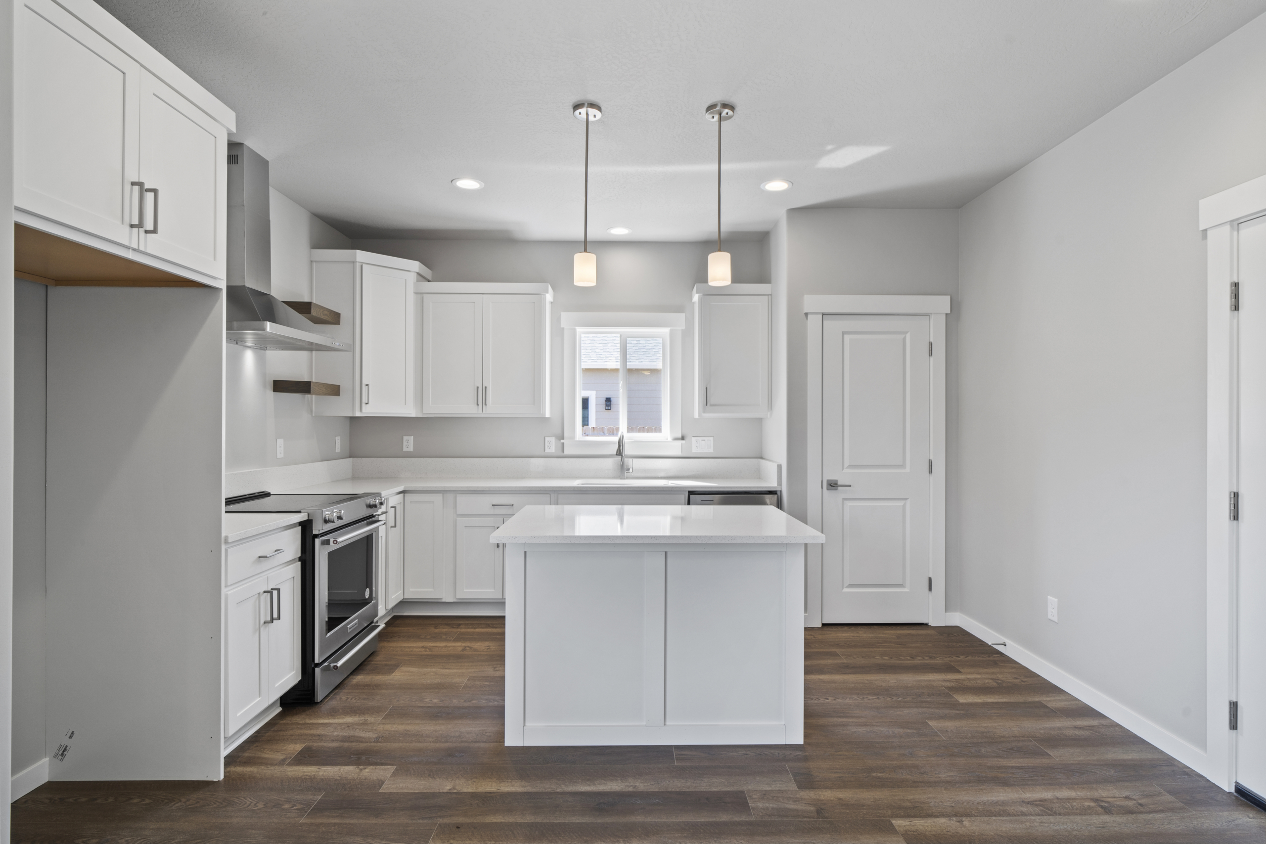 An inviting kitchen with sleek white countertops and modern stainless-steel appliances, including a prominent oven. Natural light streams in through a charming window, adding warmth to the space."